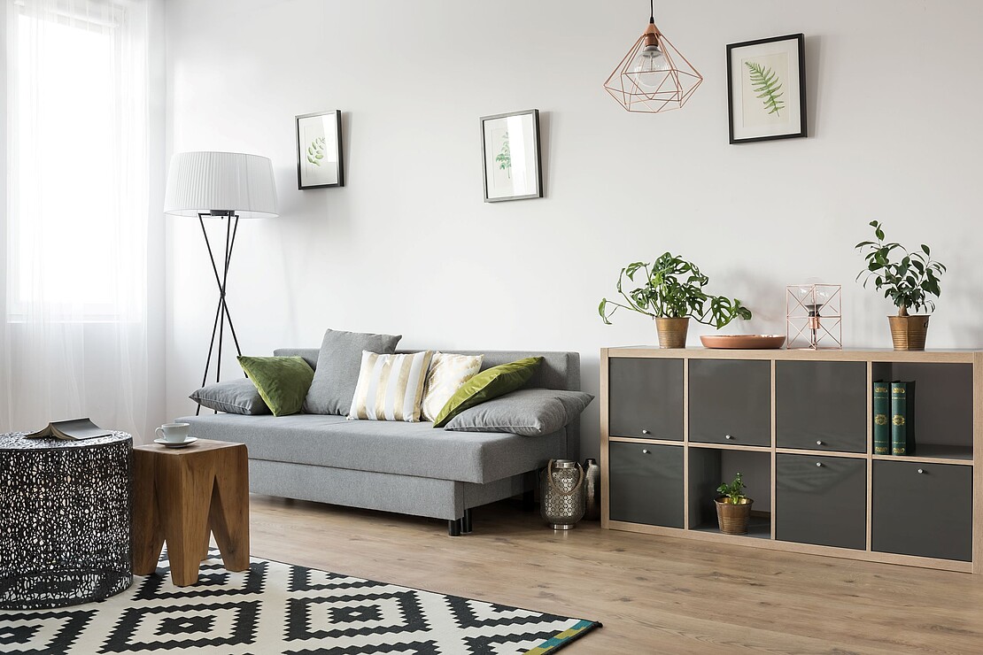 Stilvolles Wohnzimmer mit grünen Akzenten und moderner Einrichtung Ein gemütlich eingerichtetes Wohnzimmer mit grauem Sofa, grünen Kissen, Pflanzen und modernen Dekoelementen.