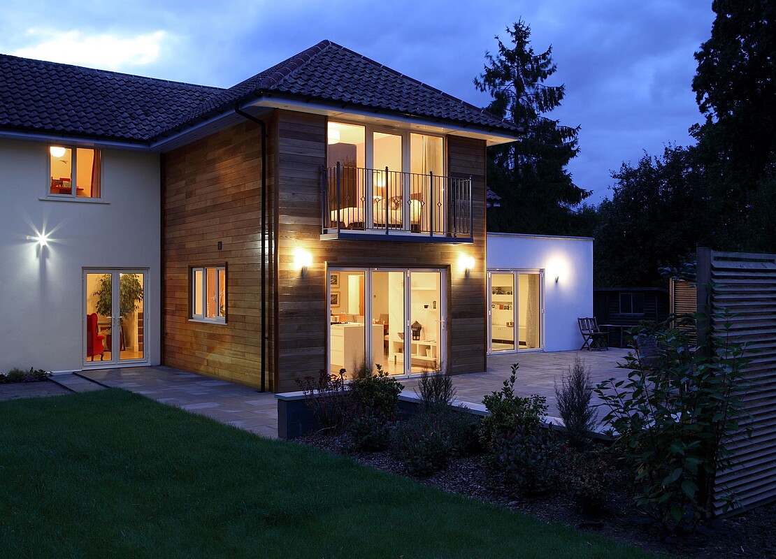 Modernes Haus bei Nacht mit warmem Licht und Holzfassade Ein modernes zweistöckiges Haus mit Holzfassade und beleuchteten Fenstern in der Abenddämmerung.